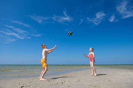 Happy children playing with ball on beach at summer sunny day with blue sky on backgroundの写真素材