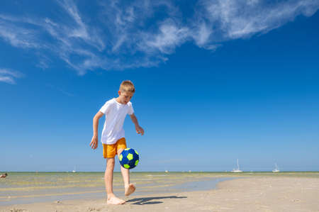Happy teen boy playing with ball on beach at summer sunny day with blue sky on backgroundの写真素材