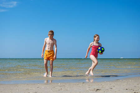 Happy children playing with ball on beach at summer sunny day with blue sky on backgroundの写真素材