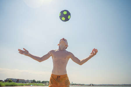 Portrait of teen boy playing volleyball with ball on beach with sunlight on background at summer sunny dayの写真素材