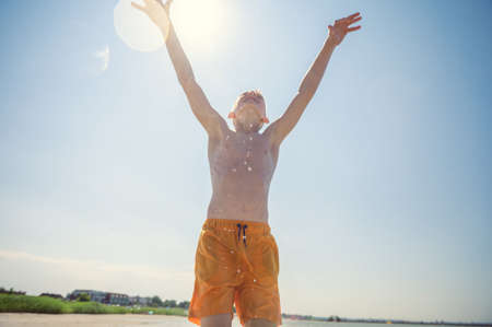 Portrait of teen boy playing volleyball with ball on beach with sunlight on background at summer sunny dayの写真素材