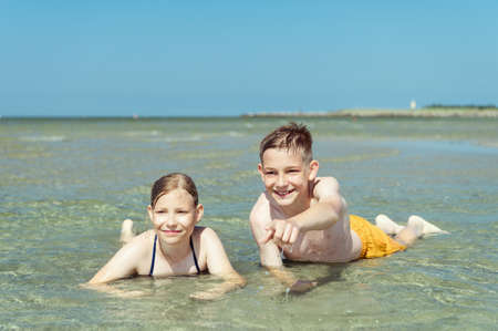 Portrait of two happy siblings teen children liying in water of baltic sea beach at summer holidaysの写真素材