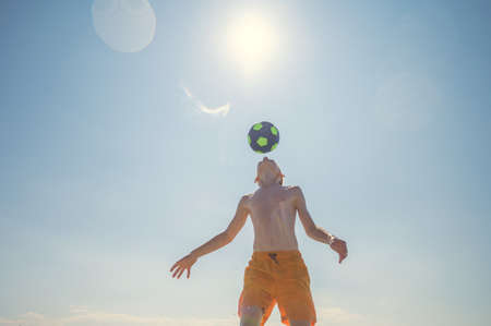 Portrait of teen boy playing volleyball with ball on beach with sunlight on background at summer sunny dayの写真素材
