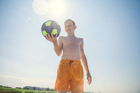 Portrait of teen boy playing volleyball with ball on beach with sunlight on background at summer sunny dayの写真素材