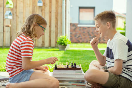 Two happy children playing chess on backyard at sunny day while summer holidaysの写真素材