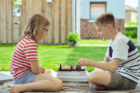Two happy children playing chess on backyard at sunny day while summer holidaysの写真素材