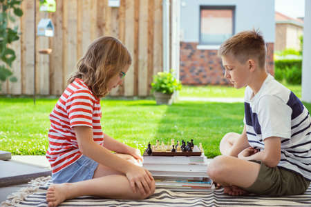 Two happy children playing chess on backyard at sunny day while summer holidaysの写真素材