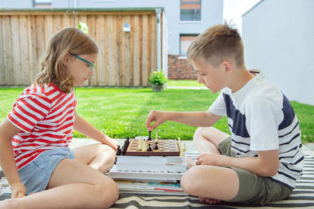Two happy children playing chess on backyard at sunny day while summer holidaysの写真素材