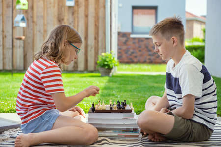 Two happy children playing chess on backyard at sunny day while summer holidaysの写真素材