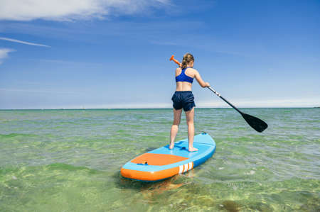 Cute little girl ecercise paddling on SUP board in sea on beautiful sunny summer day while summer holidaysの写真素材