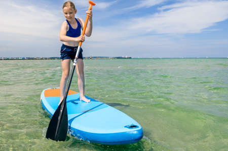 Cute little girl ecercise paddling on SUP board in sea on beautiful sunny summer day while summer holidaysの写真素材