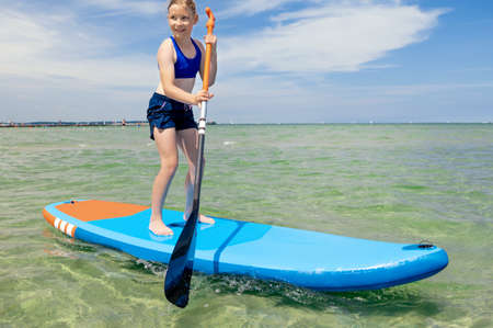 Cute little girl ecercise paddling on SUP board in sea on beautiful sunny summer day while summer holidaysの写真素材