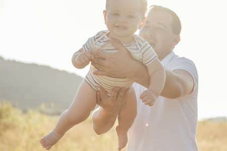 Happy young father holding toddler son and play with him as airplane flying above the field at sunny...