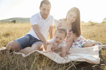 Portrait of happy young family with baby son playing and having fun together in nature during sunset on fieldの写真素材
