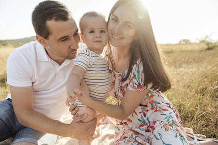 Portrait of happy young family with baby son playing and having fun together in nature during sunset on fieldの写真素材