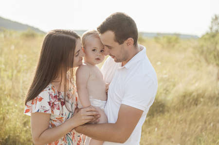 Portrait of happy young family with baby son playing and having fun together in nature during sunset on fieldの写真素材