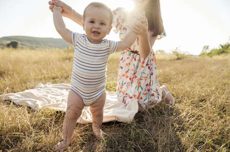 Portrait of happy young mother with her cute baby son joyful exploring the world on field at sunny dayの写真素材