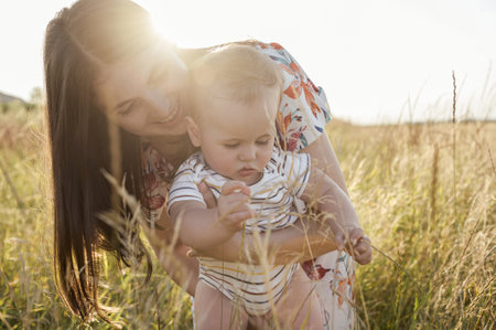 Portrait of happy young mother with her cute baby son joyful exploring the world on field at sunny dayの写真素材