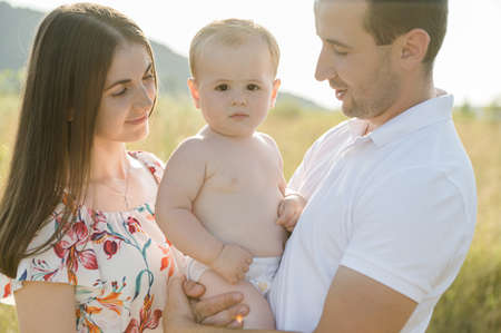Portrait of young happy family holding in hands cute toddler son enjoy sunlight at summer day on fieldの写真素材