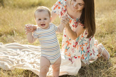 Happy pretty mother with her cute baby son enjoying summer sunlights on blanket in fieldの写真素材