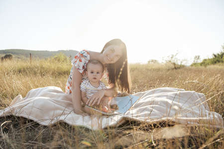 Happy pretty mother with her cute baby son enjoying summer sunlights on blanket in fieldの写真素材