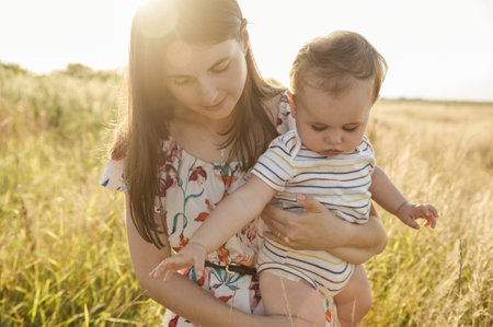 Portrait of happy young mother with her cute baby son joyful exploring the world on field at sunny dayの写真素材