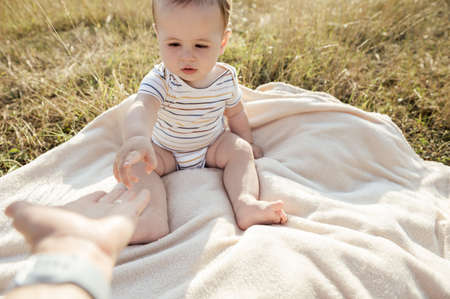 Happy adorable baby boy with beautiful eyes sitting on blanket in field with sunlight on backgroundの写真素材