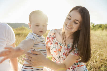 Happy pretty mother with her cute baby son enjoying summer sunlights on blanket in fieldの写真素材
