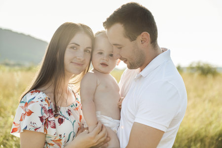 Portrait of young happy family holding in hands cute toddler son enjoy sunlight at summer day on fieldの写真素材