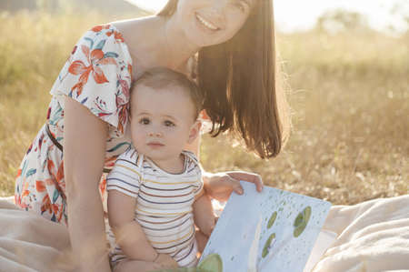 Happy pretty mother with her cute baby son enjoying summer sunlights on blanket in fieldの写真素材