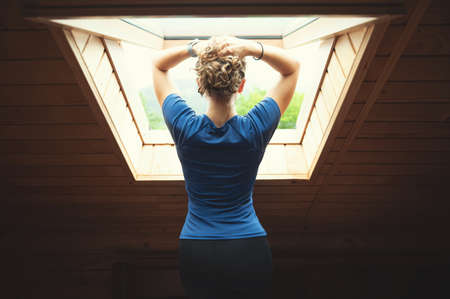 Young woman with beautiful figure and thin waist is standing by window and enjoying the morning freshness of mountainsの写真素材