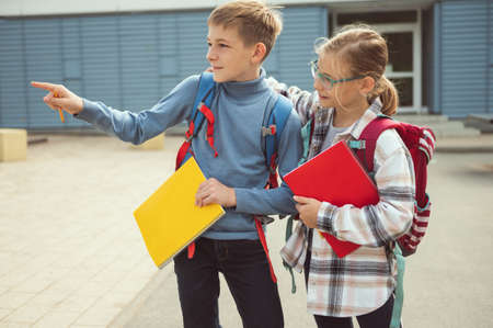 Happy preteen children with exercise books and backpacks joyfully talking after lessons at schoolyard in front of schoolの写真素材