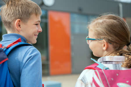 Two happy school children with backpacks walking and talking in campus before lessonsの写真素材