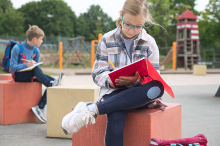 Cute teen children learning or making homework at schoolyard during break before lessonsの写真素材