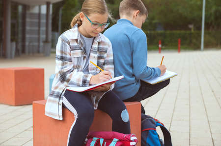 Cute teen children learning or making homework at schoolyard during break before lessonsの写真素材