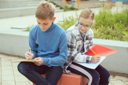 Cute teen children learning or making homework at schoolyard during break before lessonsの写真素材