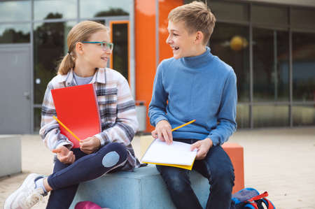 Happy teenagers schoolboy and schoolgirl sitting on schoolyard and joyful talking during breakの写真素材