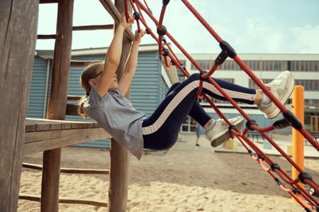 Cute little teen girl playing and climbing at playground at sunny dayの写真素材