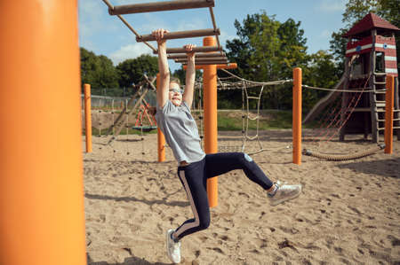 Cute little teen girl playing and climbing at playground at sunny day