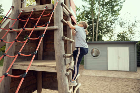 Cute little teen girl playing and climbing at playground at sunny dayの写真素材
