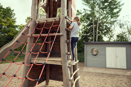 Cute little teen girl playing and climbing at playground at sunny dayの写真素材