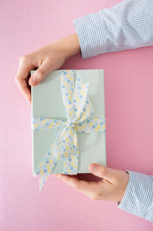 Flat lay photo of beautiful wrapped present box and hands holding gift box on pink background