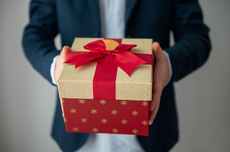 Man's hands holding elegant gift box with red bow and ribbon as christmas surpriseの写真素材