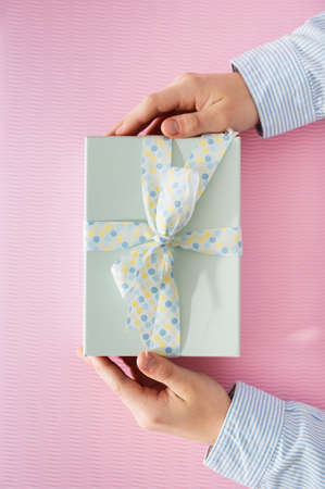 Flat lay photo of beautiful wrapped present box and hands holding gift box on pink backgroundの写真素材