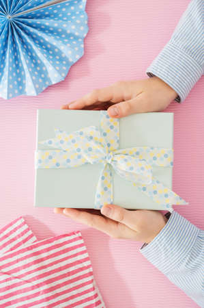 Flat lay photo of beautiful wrapped present box and hands holding gift box on pink backgroundの写真素材