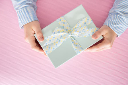 Flat lay photo of beautiful wrapped present box and hands holding gift box on pink backgroundの写真素材