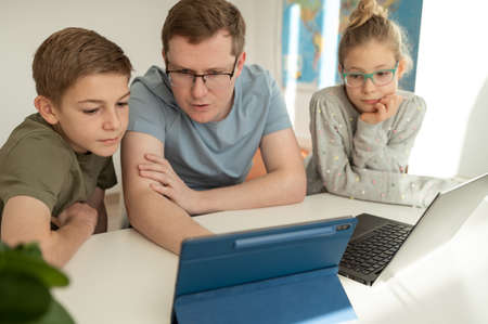 Happy young father studying with teenage children using laptop at home schoolingの写真素材