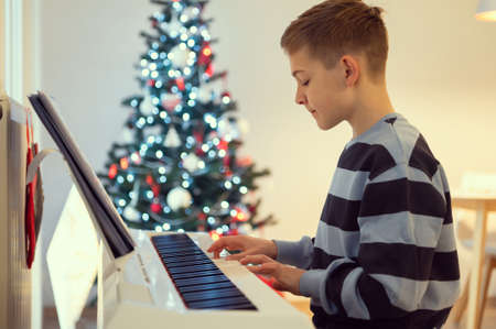 Tennage boy practise plaing piano at home with new years tree on backgroundの写真素材