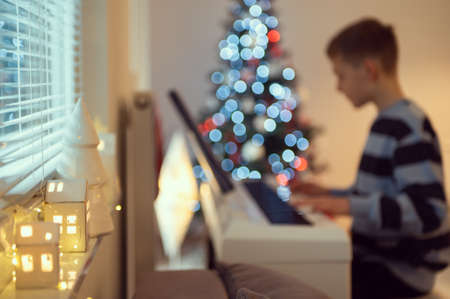 Tennage boy practise plaing piano at home with new years tree on backgroundの写真素材