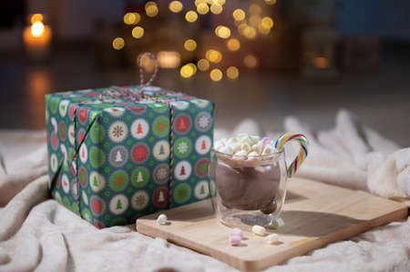 Cozy photo of cup of hot chocolate with marshmallows and christmas gift box with bokeh lights on backgroundの写真素材